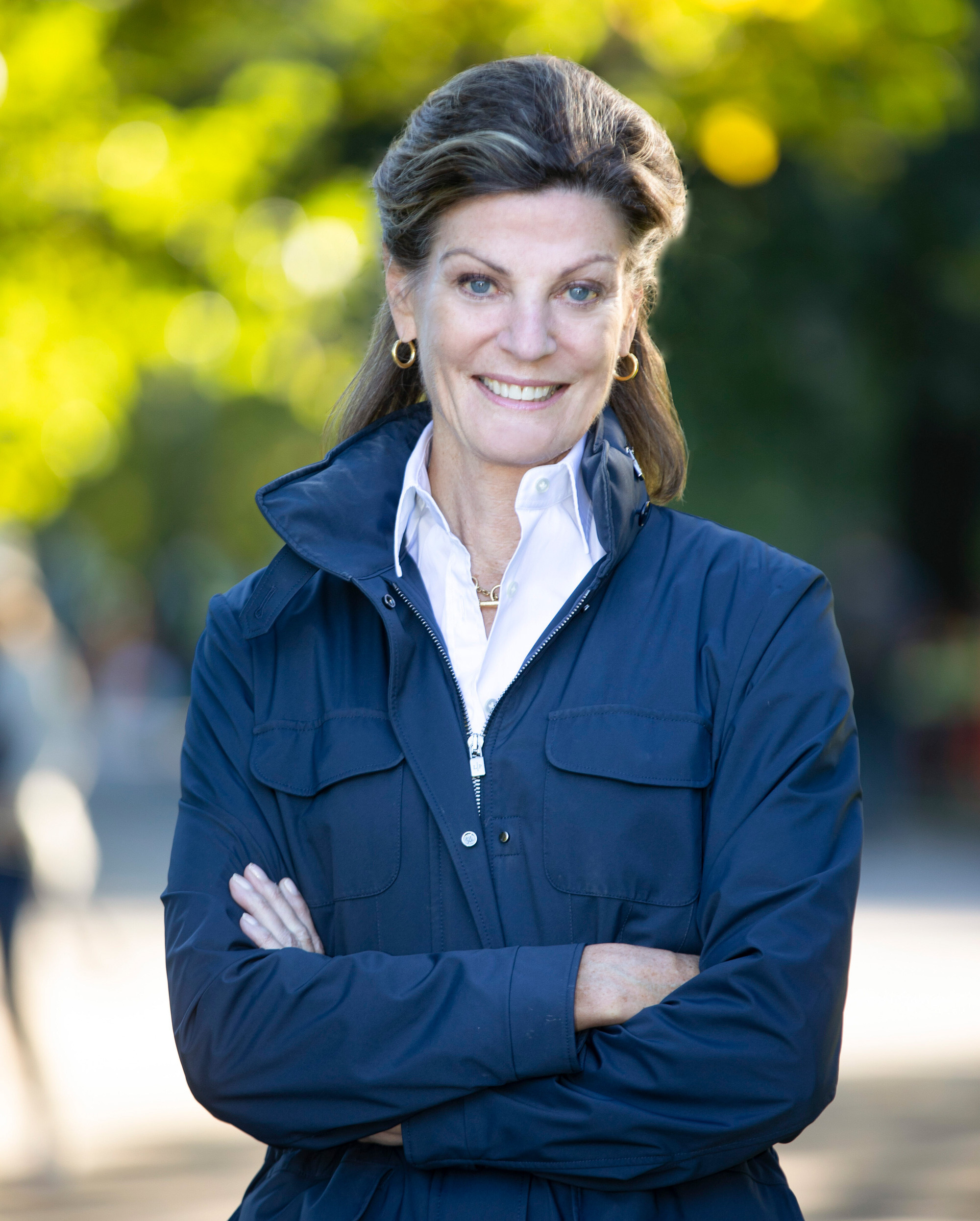 Betsy Smith, President & CEO of Central Park Conservancy, smiling and standing with arms crossed outdoors in Central Park, wearing a blue jacket.