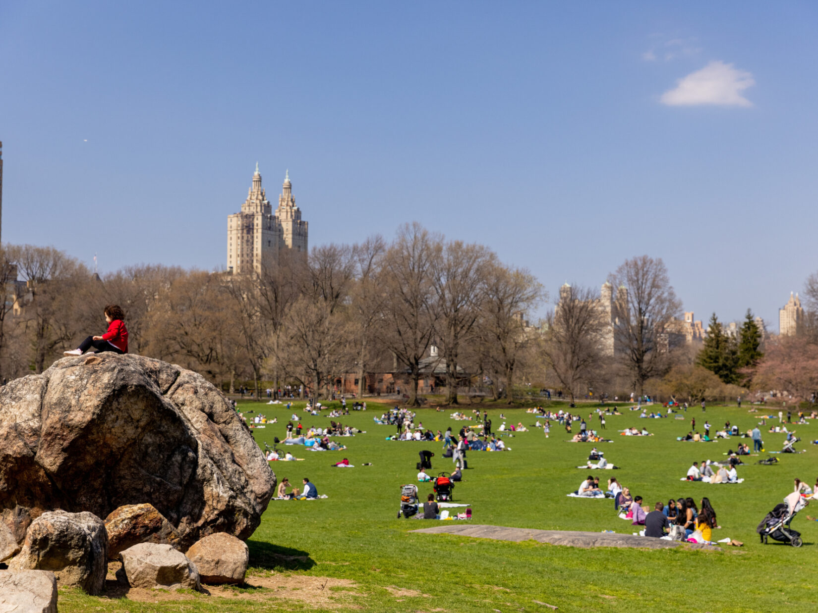 Park-goers on the Sheep Meadow enjoying a crisp Fall day. One visitor sits atop a large boulder.